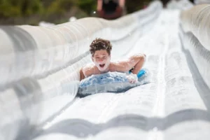 Teen coming down water slide on raft with suds