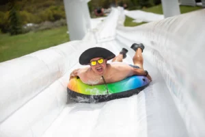 man with hat and sunglasses coming down water slide on tube